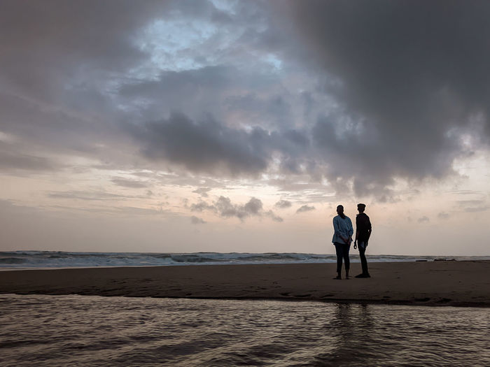 Men standing on beach against sky during sunset