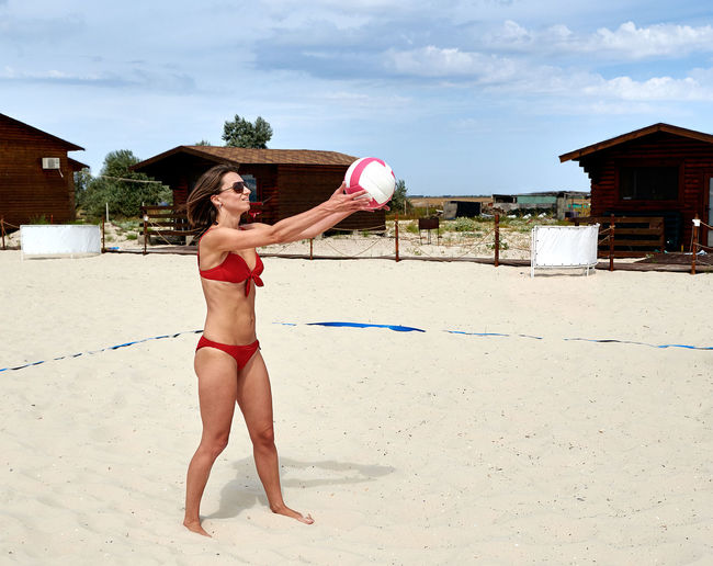 Woman in bikini playing volleyball at beach against sky