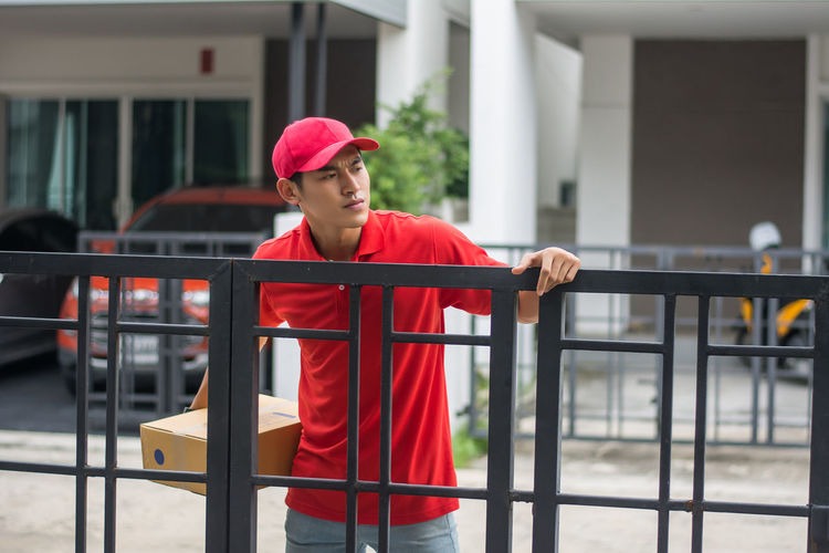 Delivery man standing at closed gate against buildings