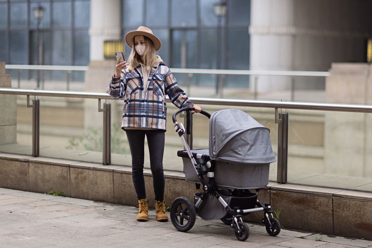 Happy mother walking with stroller in park and using mobile phone. joy of motherhood. stylish woman