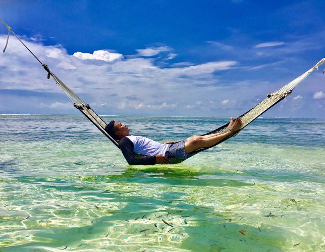 Man relaxing in hammock over sea against sky