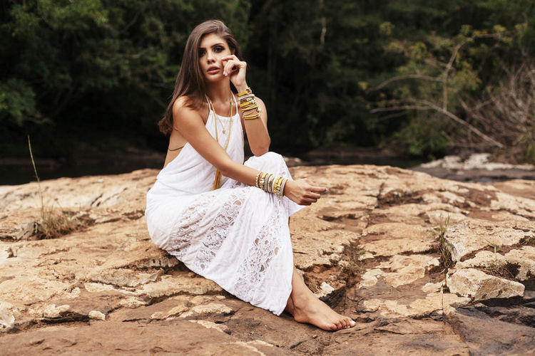Young woman wearing dress sitting on rock formation at forest