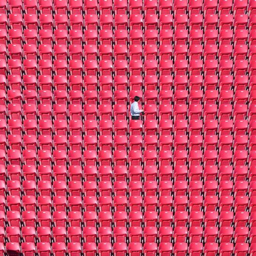 Man standing amidst red chairs at stadium