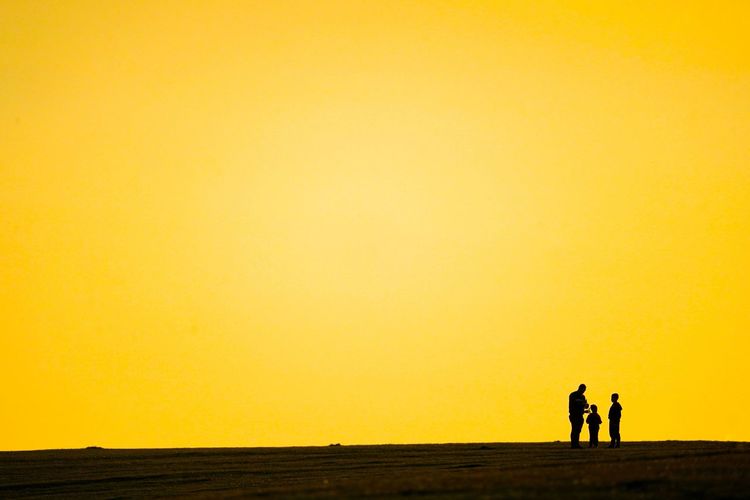Silhouette people walking on fields against orange sky