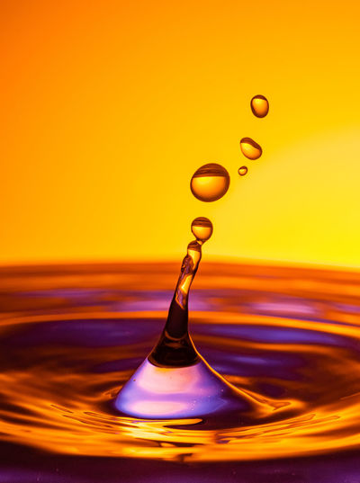 Close-up of drop falling on water against orange background