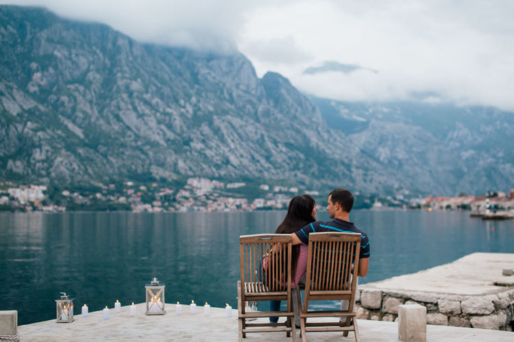 Rear view of couple sitting on lake against mountains