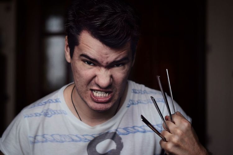 Portrait of angry man with spoons amidst fingers at home