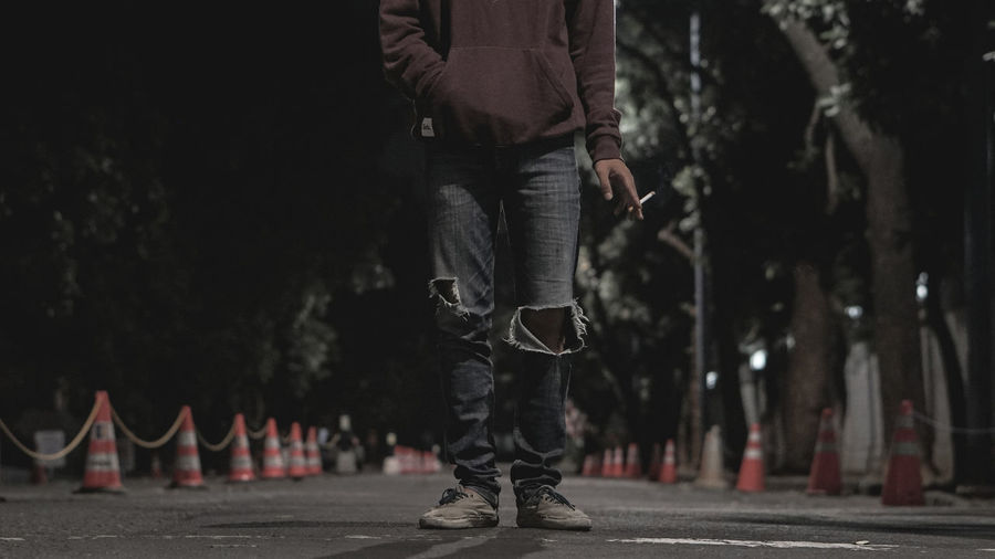 Low section of man smoking cigarette while standing on road at night