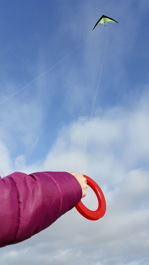 Cropped hand flying kite in blue sky