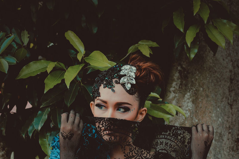 Young woman with scarf covering mouth looking away against tree trunk