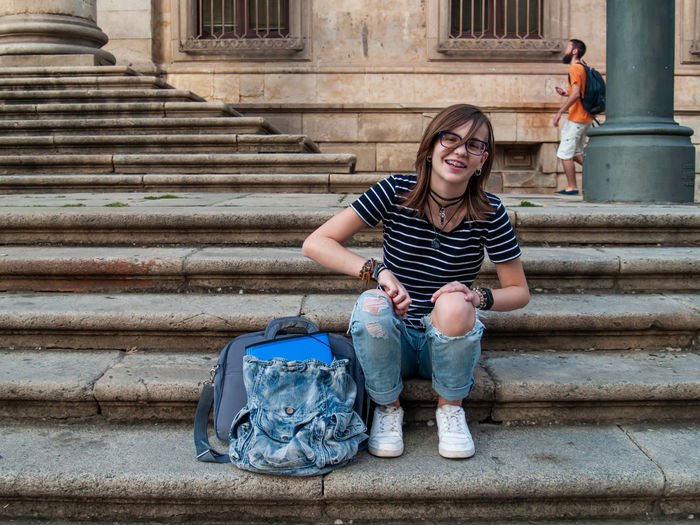 Full length portrait of smiling teenage girl sitting on steps