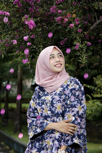 Smiling young woman in hijab standing against plants