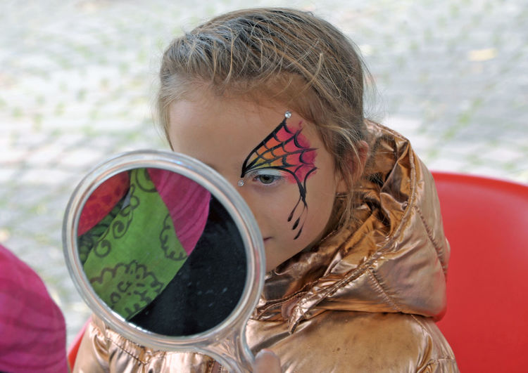 Close-up of girl with face paint looking in mirror