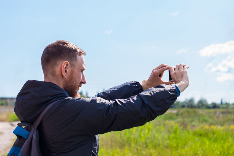 Side view of man photographing against sky