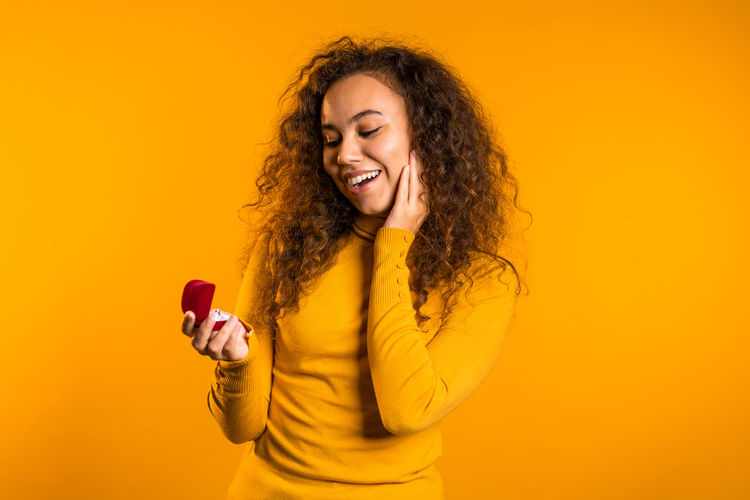 Portrait of a smiling young woman using phone against yellow background