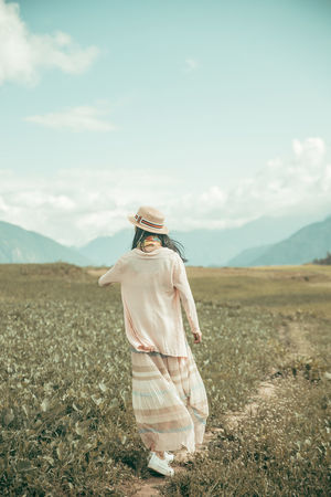 Rear view of woman walking on footpath amidst field against sky