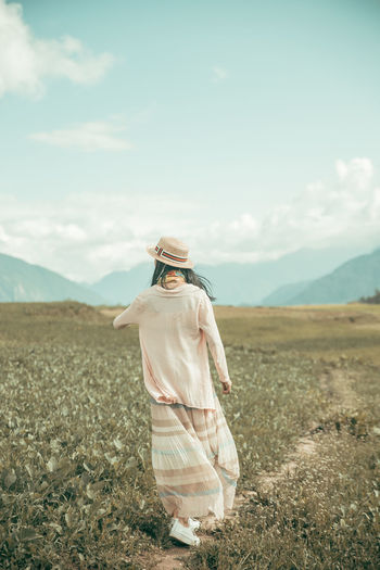 Rear view of woman walking on footpath amidst field against sky