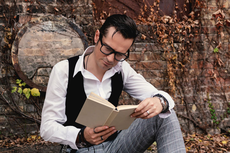 Retro-styled man reading book while relaxing outdoors.