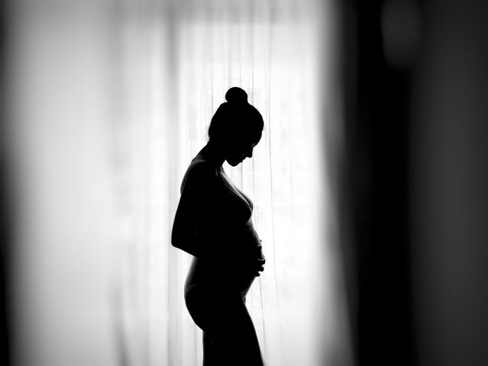 Side view of silhouette pregnant woman standing by window at home
