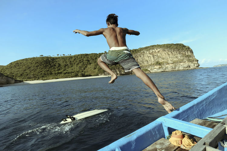 Full length of shirtless man jumping in sea against sky