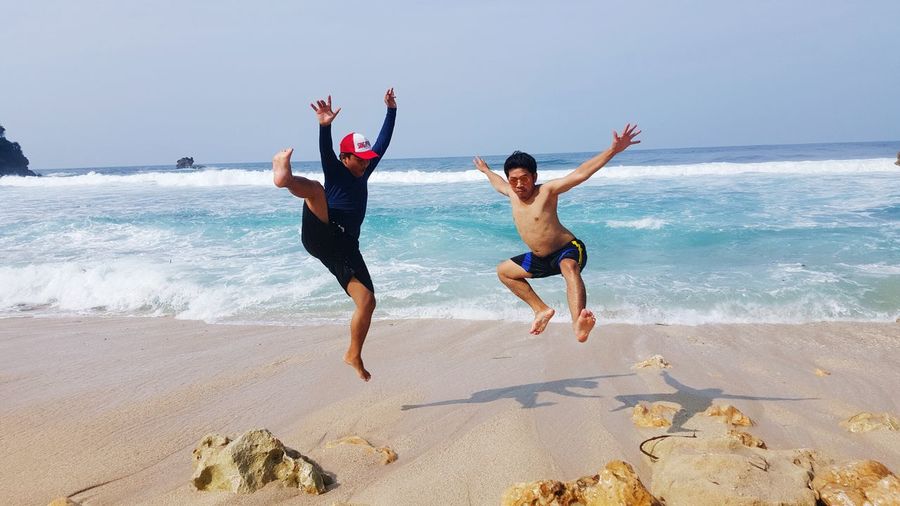 Full length of playful friends jumping at sandy beach