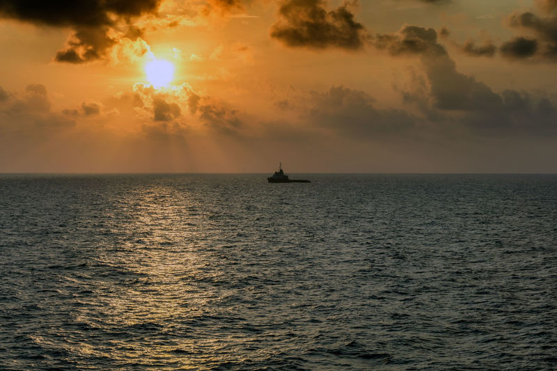 A silhouette of an anchor handling tugboat maneuvering during sunset at offshore oil field