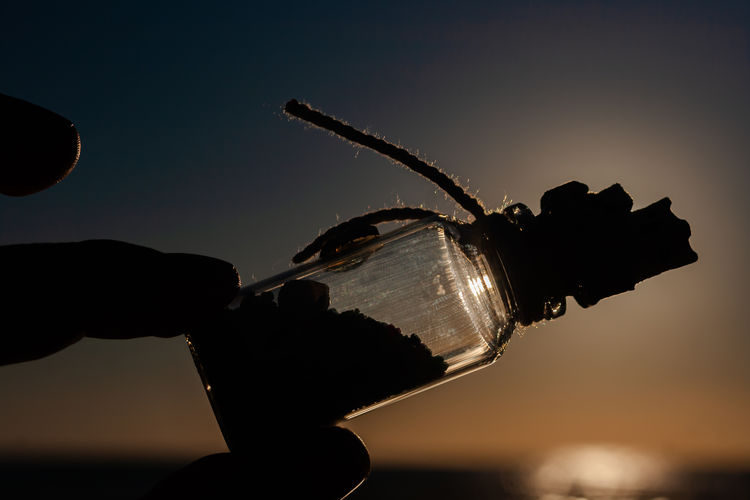 Close-up of silhouette hand against sky during sunset