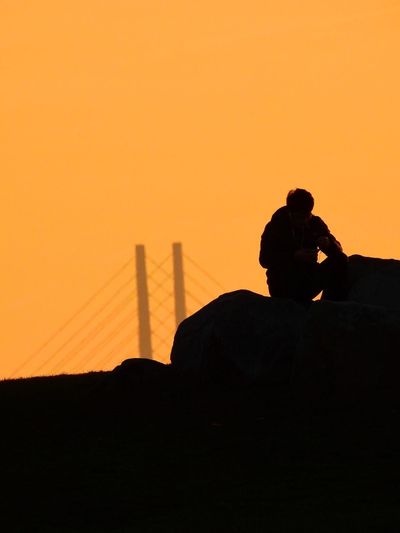 Silhouette man photographing on landscape against orange sky
