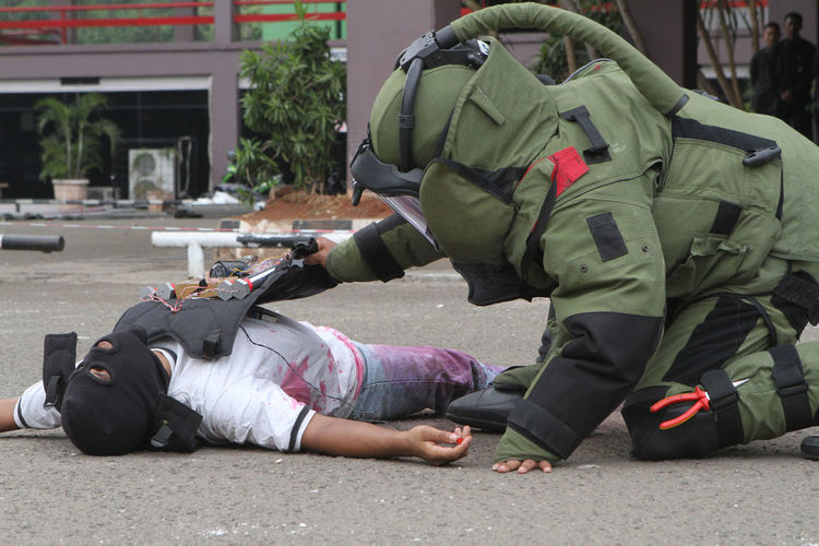 Military soldier defusing bomb on criminal body on street
