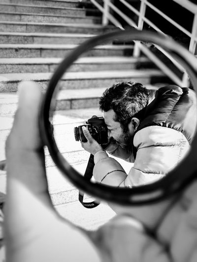 Man photographing with camera seen through loop held by women
