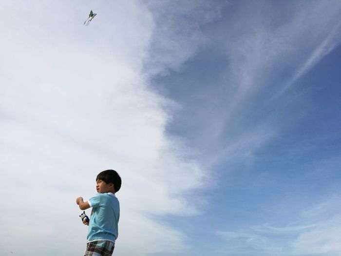 Low angle view of boy flying kite against cloudy sky