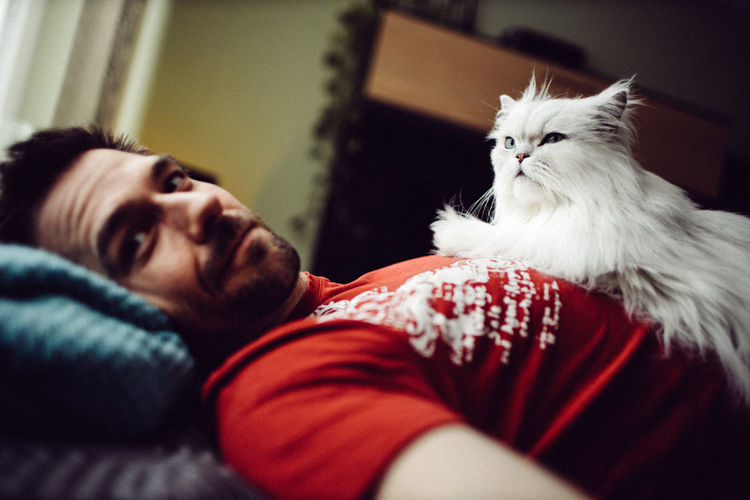 Portrait of man with cat relaxing on bed at home