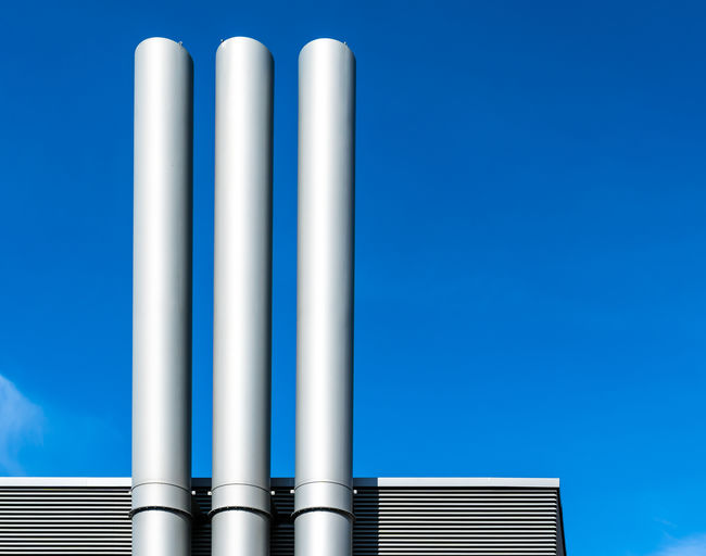 Low angle view of smoke stacks at factory against blue sky