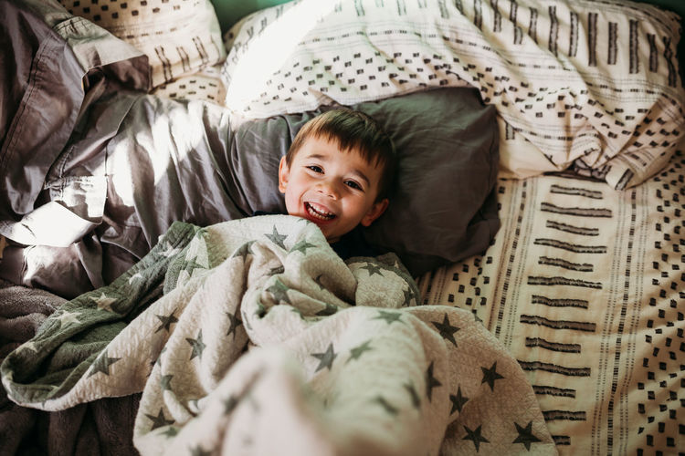 Young boy laying in bed in morning light laughing