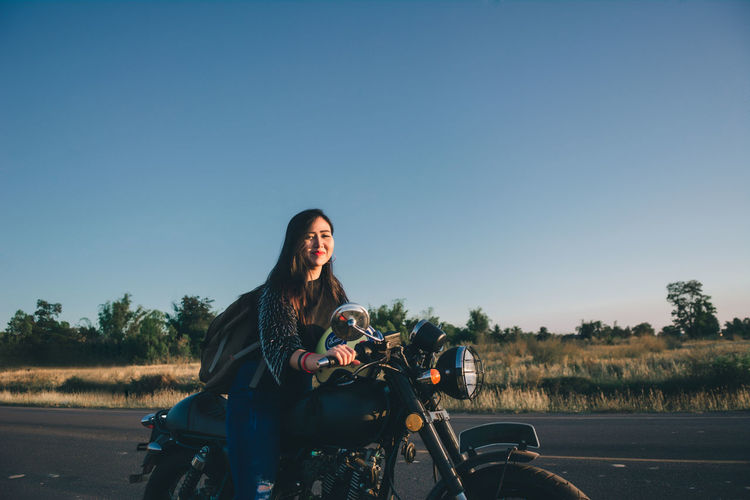 Portrait of young woman sitting on motorcycle against clear sky