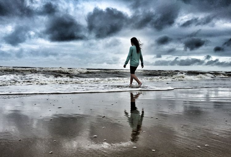 Man standing on beach against cloudy sky