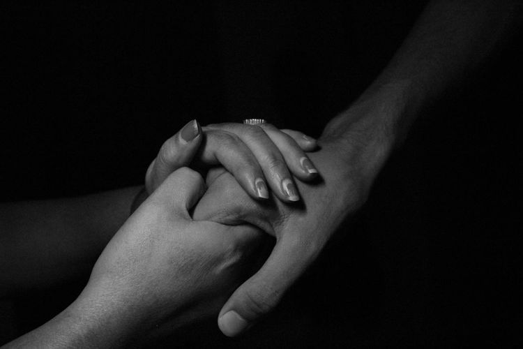 Cropped image of couple holding hands against black background