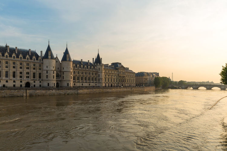 Conciergerie by river in city against sky during sunset
