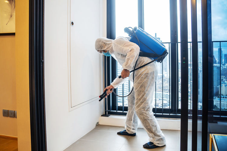 Full length of man wearing protective suit sanitizing home
