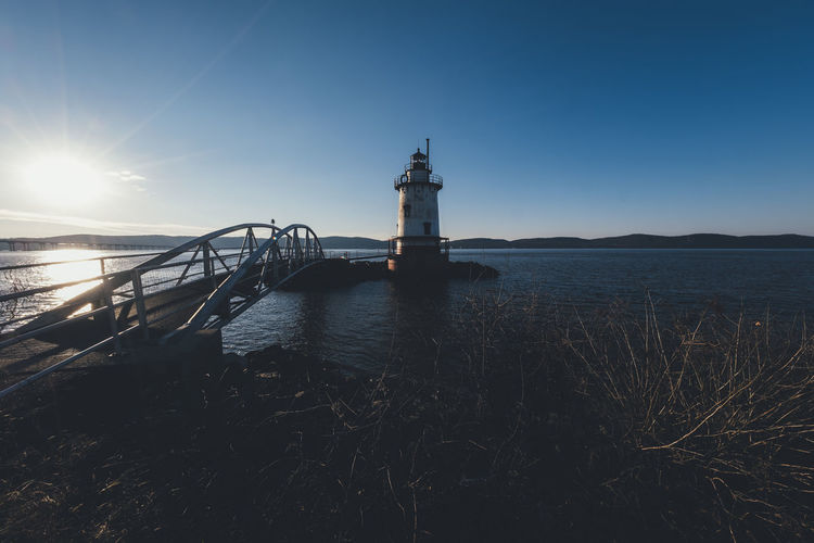Bridge over sea by lighthouse against clear sky