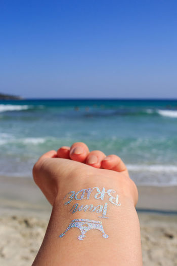 Cropped hand of woman with temporary tattoo against sea