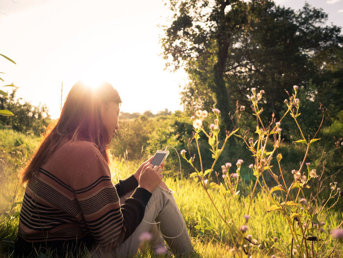 Rear view of woman using mobile phone on field