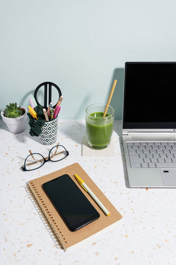 Laptop, healthy green juice, book, mobile phone and succulent plant over desk at home