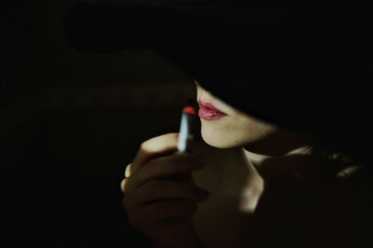 Close-up of woman applying lipstick against black background