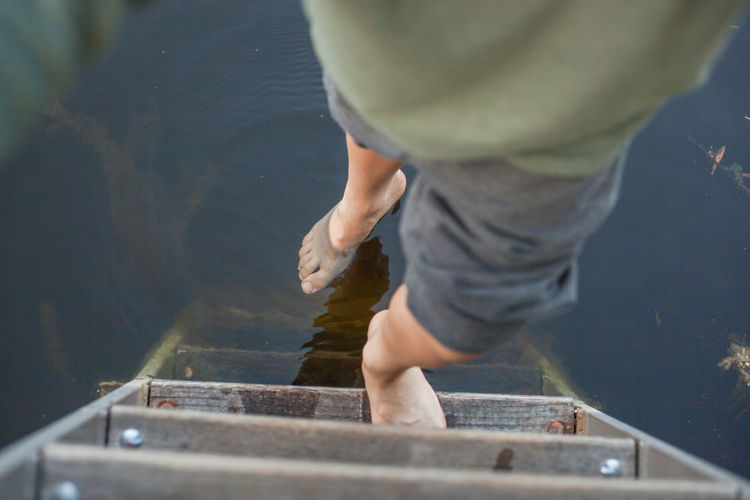 Low section of boy standing on wooden ladder over lake