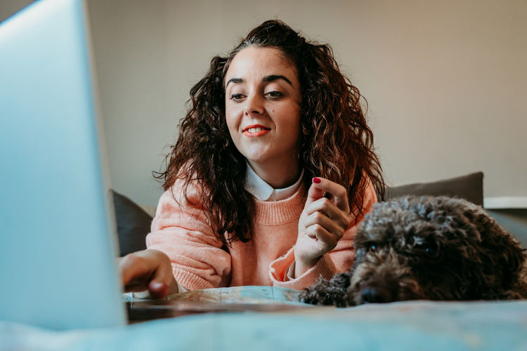 Smiling woman using laptop by dog on bed at home