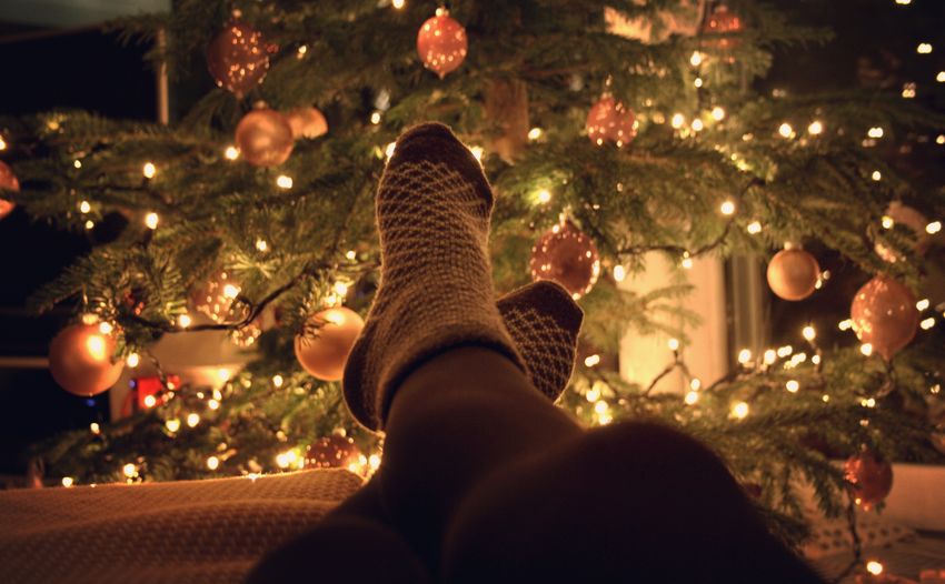 Low section of person relaxing in front of illuminated christmas tree