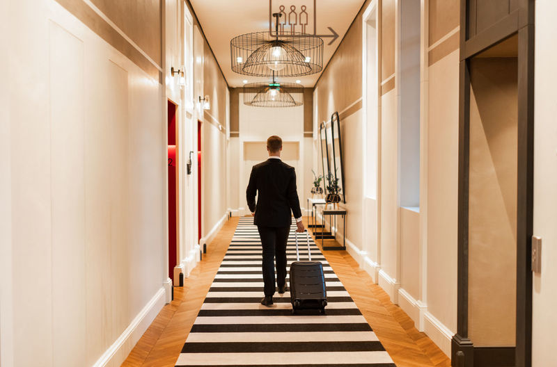 Unrecognizable entrepreneur with luggage in hotel corridor