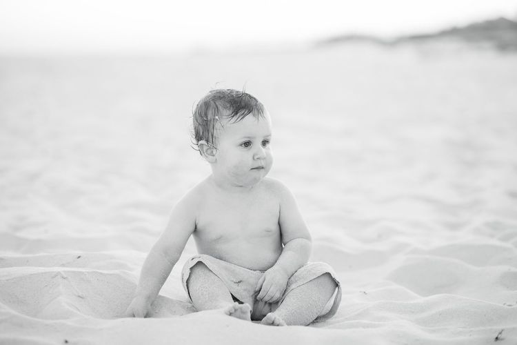 Cute baby boy sitting on sand at beach