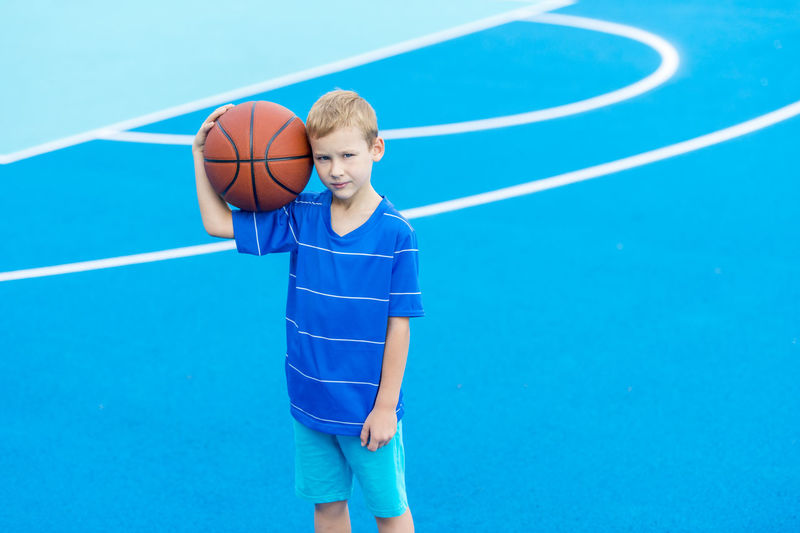 Portrait of boy holding basketball while standing at court